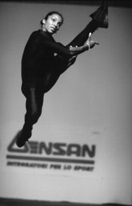 Athlete performing a high kick in front of a sponsor banner