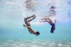 Two swimmers diving over a sandy sea bed, arena Water Instinct S/S 2018 catalogue